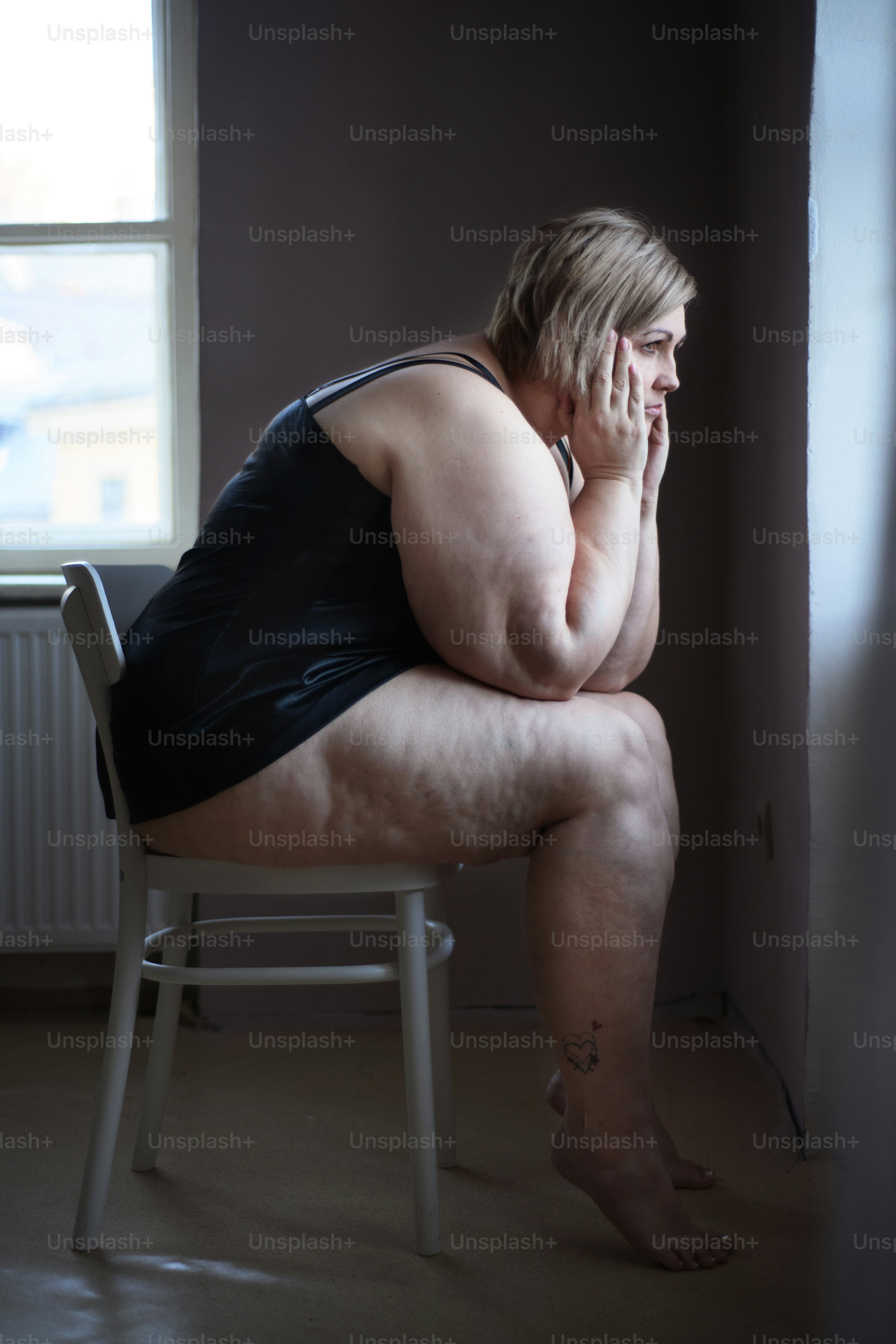 Depressed lonely fat woman sitting and looking through the window at home at dark